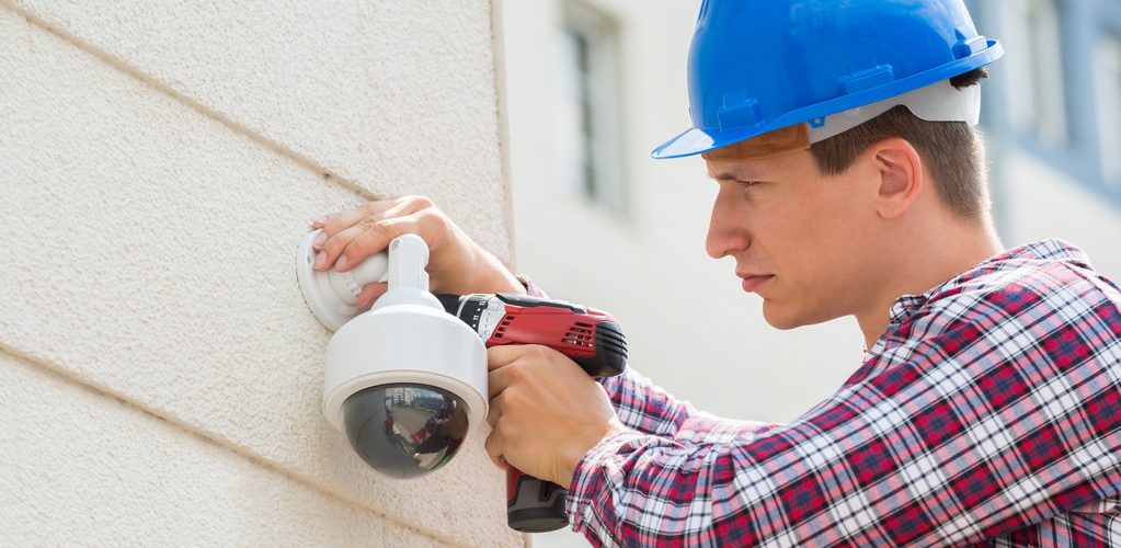 Young Male Technician Installing Camera On Wall